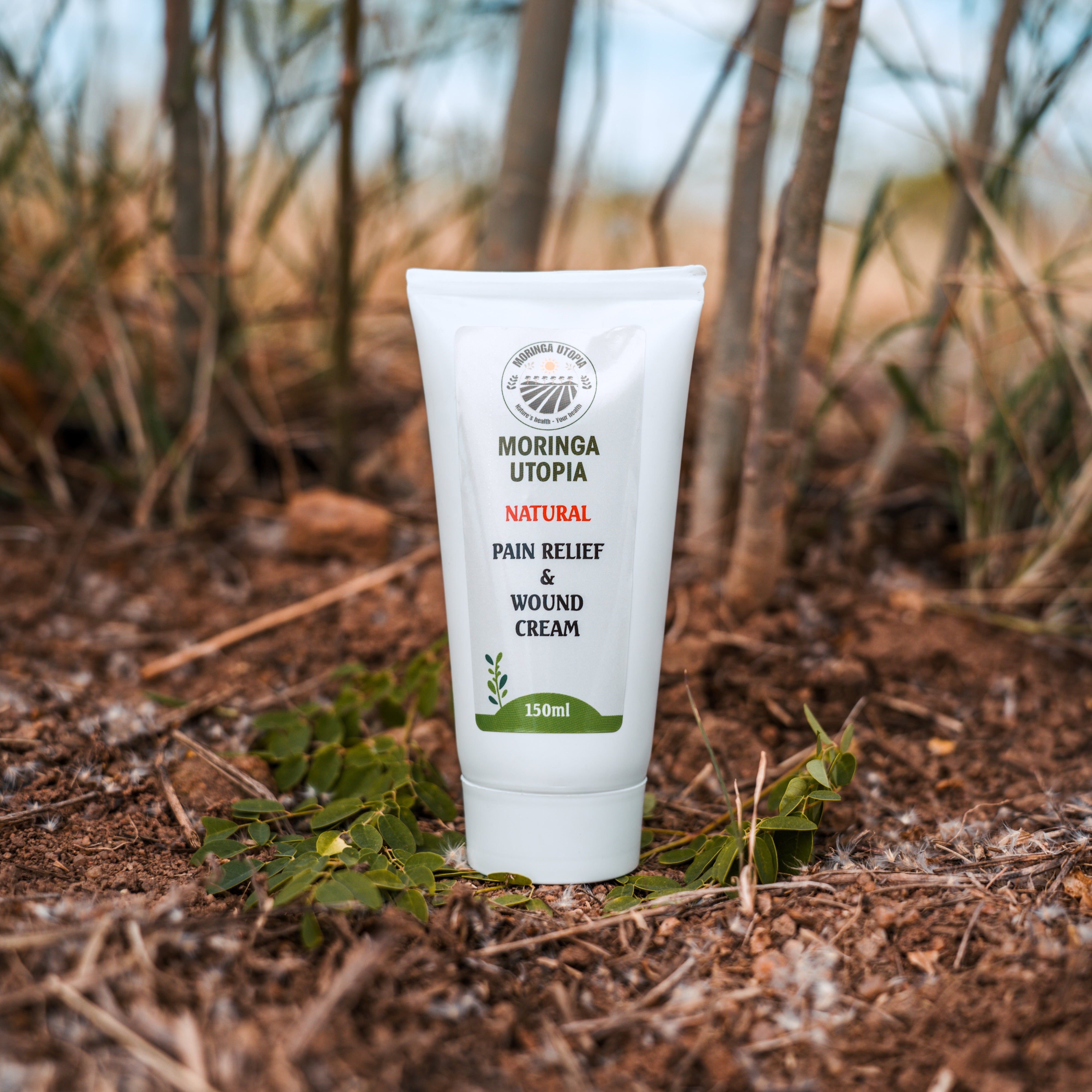 Tube of Moringa Utopia natural pain relief and wound cream on the ground with plants in the background